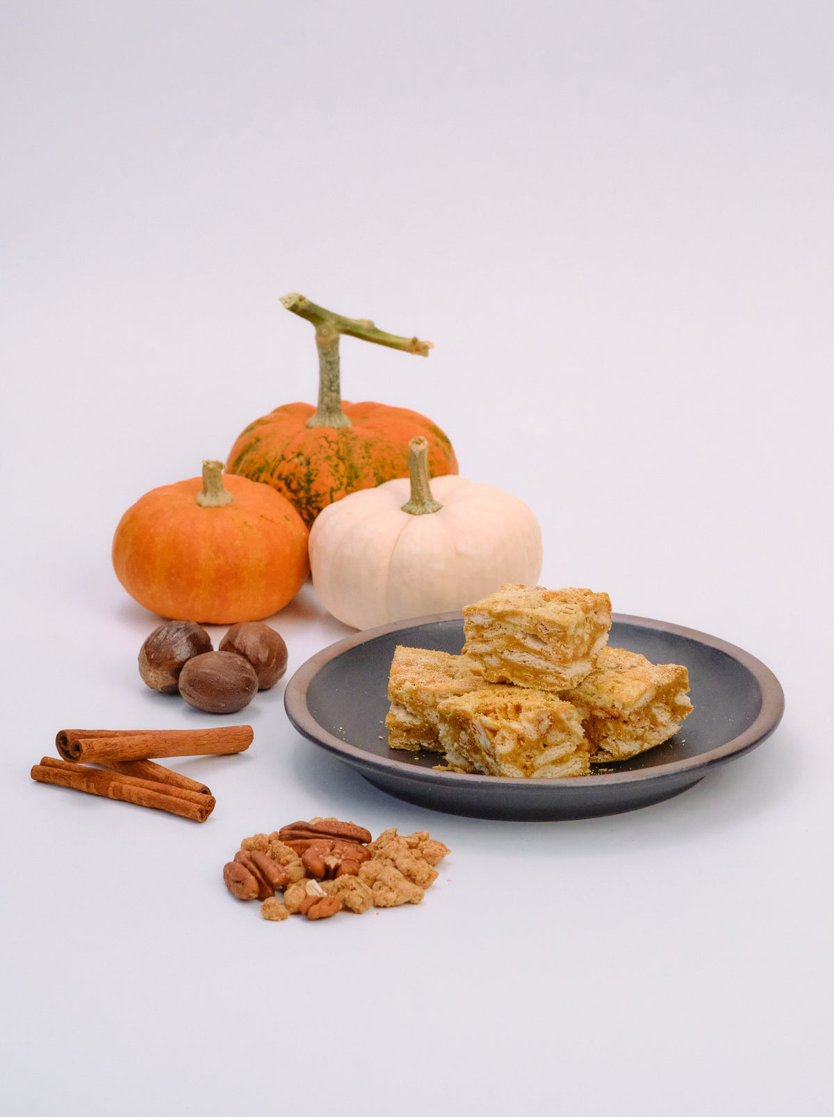 Pumpkin Pie Snowcubes stacked on a dark plate beside small pumpkins, cinnamon sticks, nutmeg, and pecans