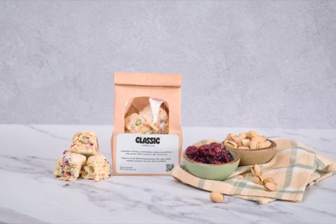 牛皮纸 Snowcubes Classic 小袋放在大理石台面上，旁边有堆叠的小块、蔓越莓干、开心果和格纹布