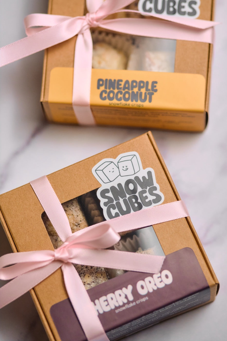 Two Snowcubes gift boxes tied with pink ribbons, showing Pineapple Coconut and Cherry Oreo labels
